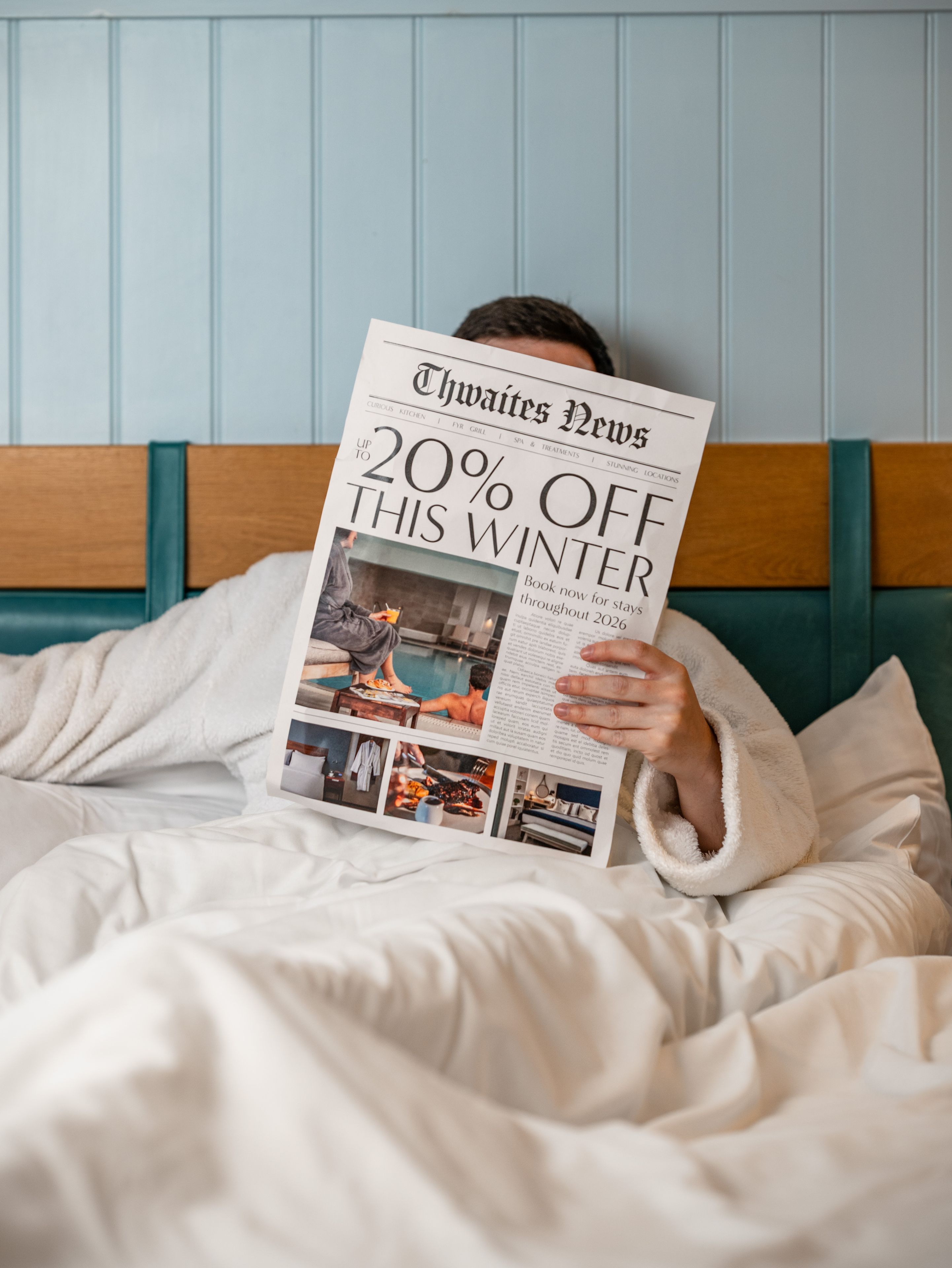 Person in hotel bed with newspaper that reads "Up to 20% off winter sale"