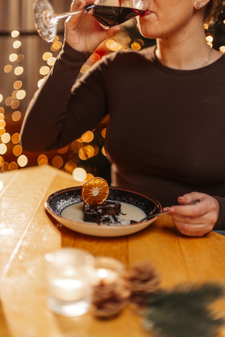 Lady eating Christmas desert with a glass of red wine